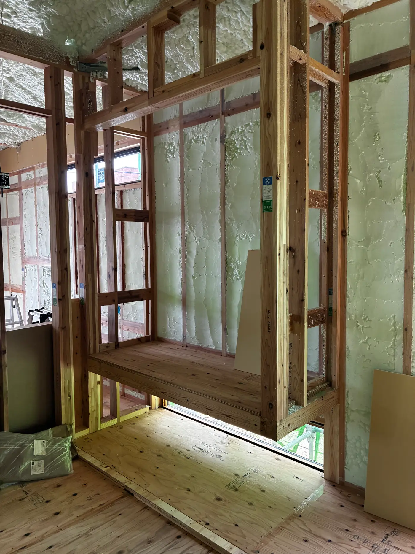Detail view of a wooden beam and header in a Japanese house frame, with sprayed foam insulation visible on the wall behind