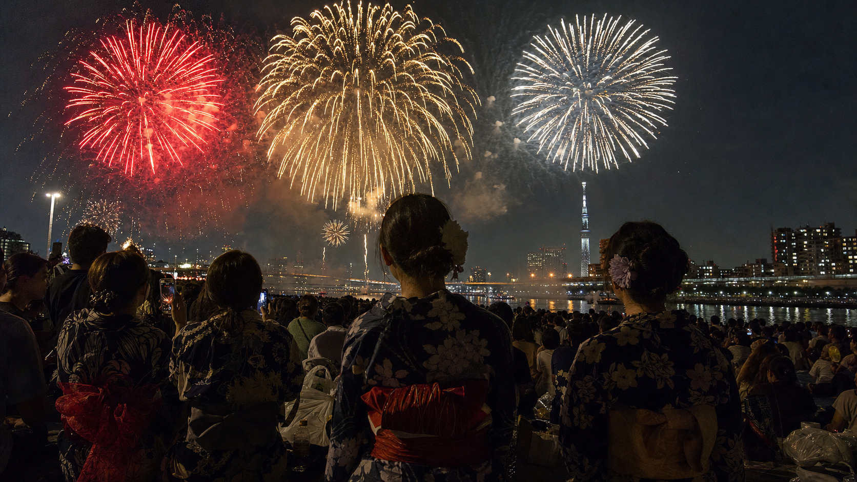 Fireworks bursting over the Sumida River in Tokyo with crowds watching from the riverbank