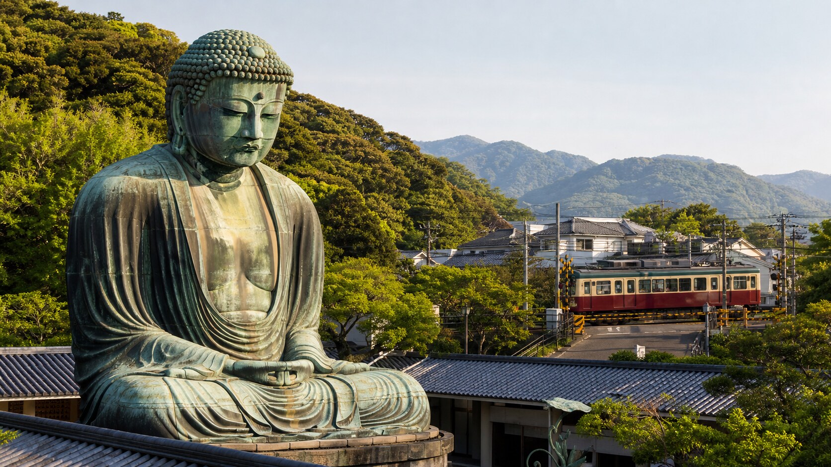 The Great Buddha of Kamakura overlooking a local train crossing with green hills in the distance